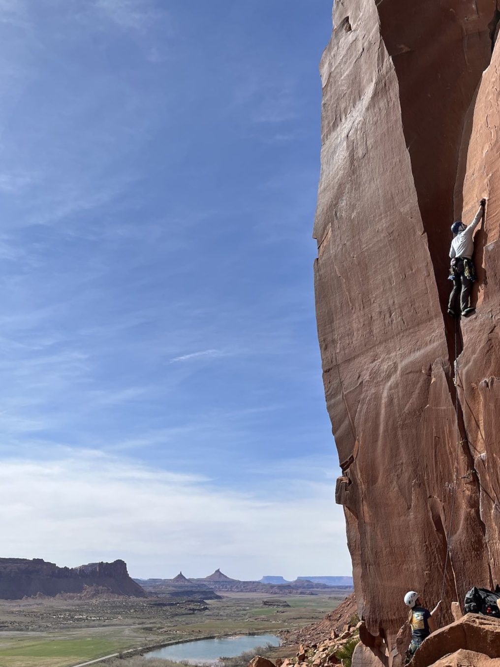 Ian crack climbing a red sandstone wall above the desert at Indian Creek, Utah